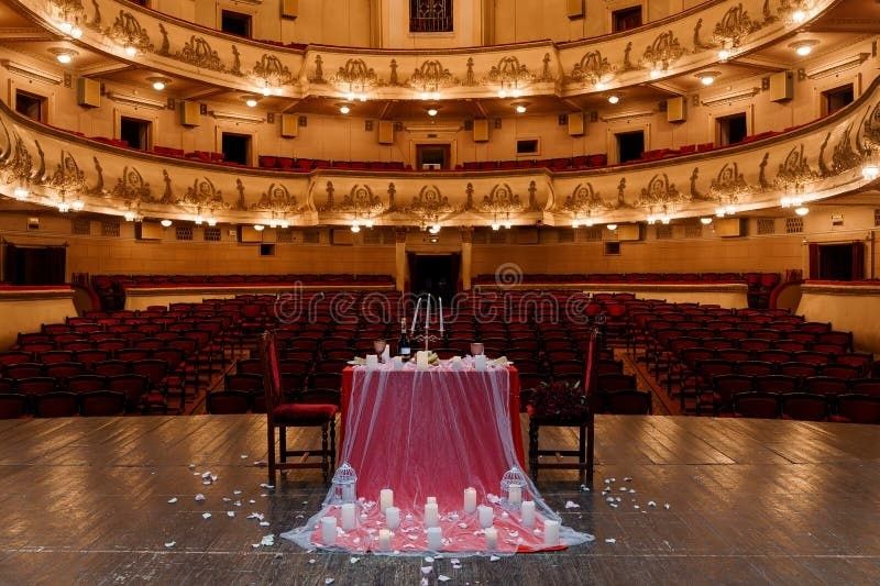 Ornate theater auditorium with a candlelit dinner table onstage