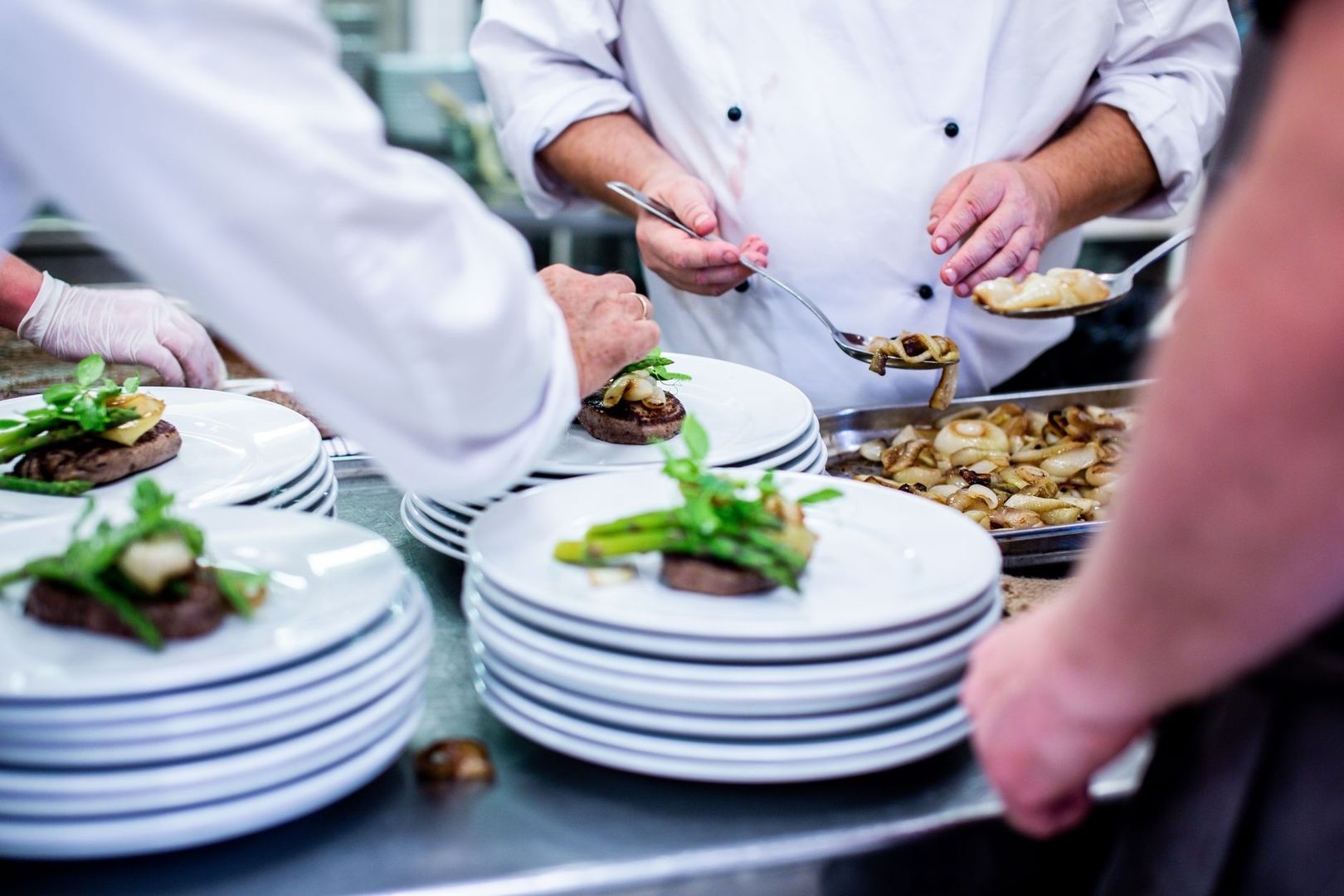 Chefs use spoons to plate garnishes and vegetables onto stacked banquet plates